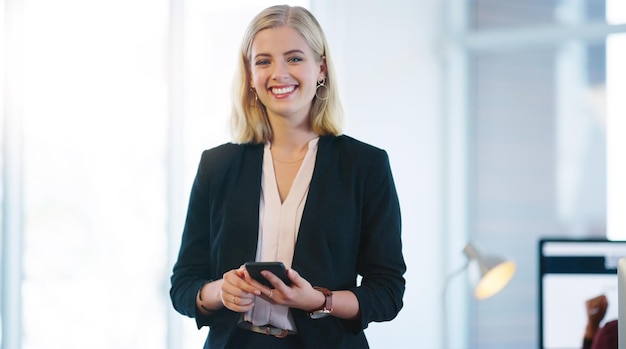 Vertrauen ist das, was Sie brauchen, um ein Unternehmen überleben zu lassen Porträt einer selbstbewussten jungen Geschäftsfrau, die ihr Mobiltelefon hält, während sie im Büro steht