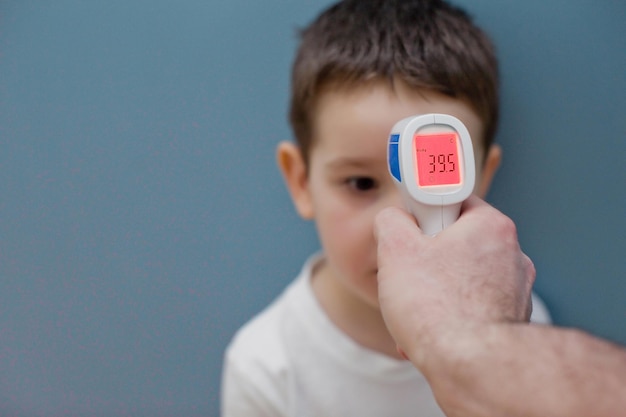 Verwenden Sie ein Infrarot-Thermometer, um die Körpertemperatur des Kindes auf blauem Hintergrund zu messen