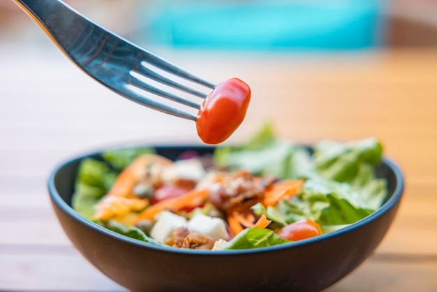 Verwenden Sie eine Gabel, einen Tomatenspieß im Vordergrund und einen Salat im Hintergrund Frühstückssalat