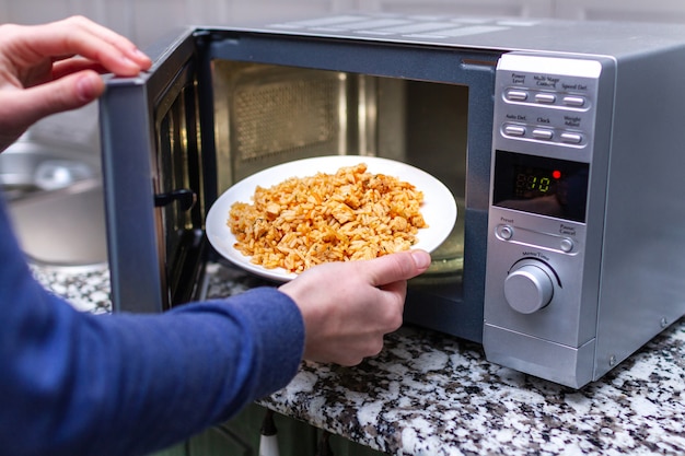 Verwenden Sie eine Mikrowelle, um einen Teller mit hausgemachtem Pilaw zum Mittagessen zu Hause zu erwärmen. Warme Mahlzeit