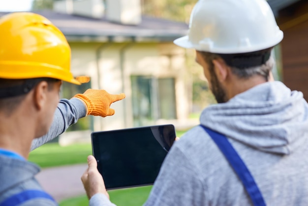 Foto verwenden sie ihre vision in der nähe von zwei jungen männlichen baumeistern, die über einen digitalen tablet-pc diskutieren