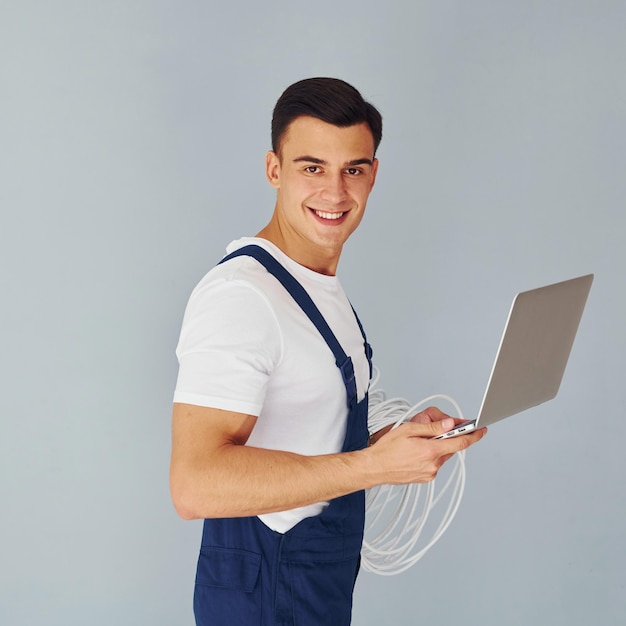 Verwendet Laptop Männliche Arbeitskraft in blauer Uniform, die innerhalb des Studios vor weißem Hintergrund steht