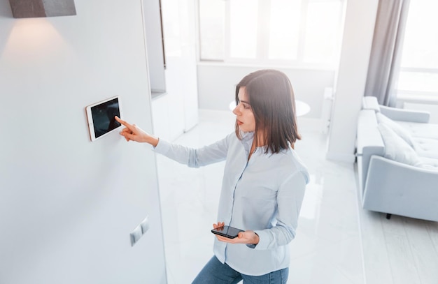 Verwendet Tablet, das in der Wand montiert ist. Junge Frau ist tagsüber im Smart House-Zimmer