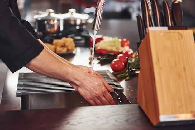 Verwendung von Geräten Professioneller junger Küchenchef in Uniform, der mit Gemüse in der Küche arbeitet