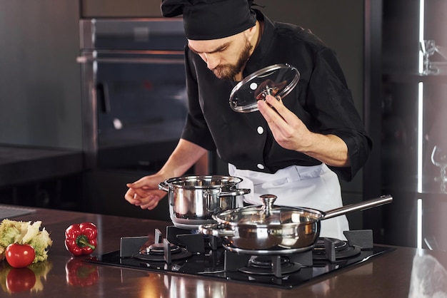 Verwendung von Geräten Professioneller junger Küchenchef in Uniform, der mit Gemüse in der Küche arbeitet