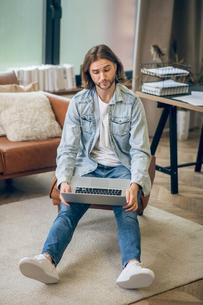 Verwirrt. Mann im Jeanshemd, der am Laptop arbeitet und verwirrt schaut