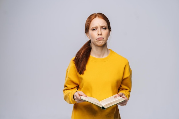 Verwirrt unzufriedene junge Studentin, die ein Buch hält und in die Kamera schaut