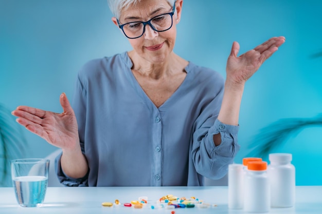 Verwirrte ältere Frau, die ihre Medikamente auf dem Tisch betrachtet Konzept der Nichteinhaltung von Medikamenten