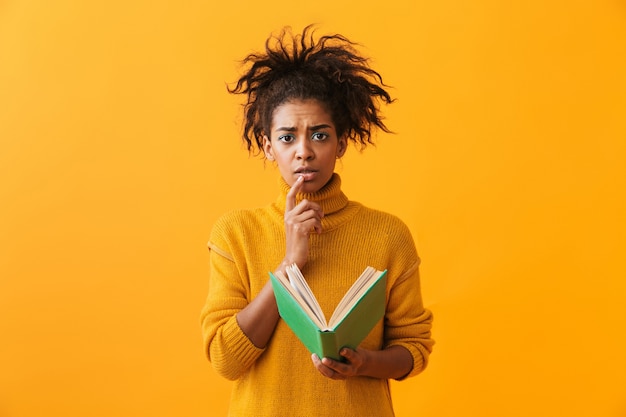 Verwirrte afrikanische Frau, die Pullover hält, der ein Buch lokalisiert hält