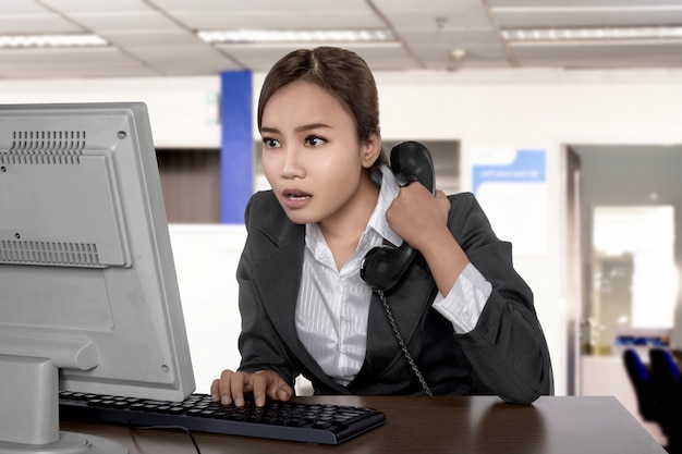 Verwirrter asiatischer tragender Anzug der Geschäftsfrau, der den Schirm beim Halten des Telefons schaut