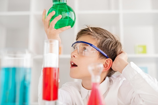 Foto verwirrter junge untersucht chemische substanz im kolben