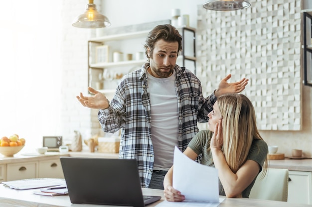 Foto verwirrter kaukasischer millennial-typ mit stoppeln breitet seine arme an den seiten aus und sieht blonde dame an