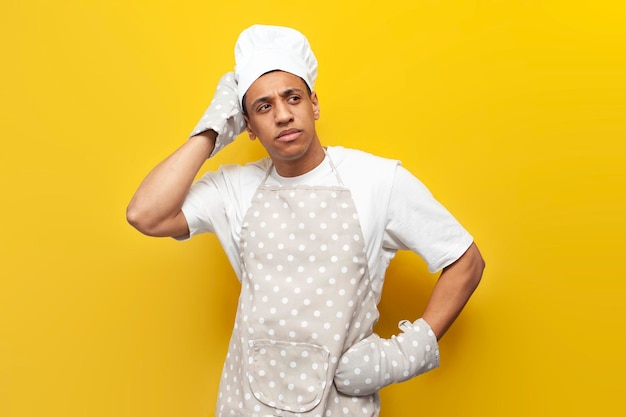 verwirrter kerl afroamerikanischer koch in uniform denkt auf gelben isolierten hintergrund bäcker in handschuhen