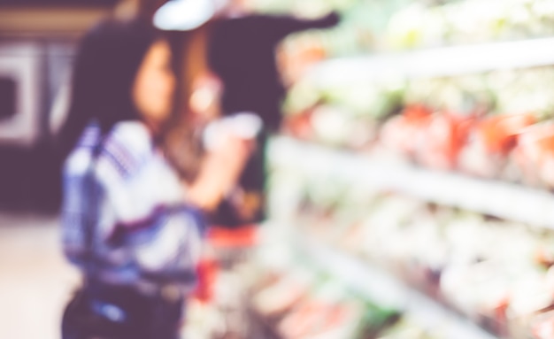 Verwischen Sie Hintergrund des Frauenkunden wählen Sie frisches Produkt auf Regal im Supermarkt aus