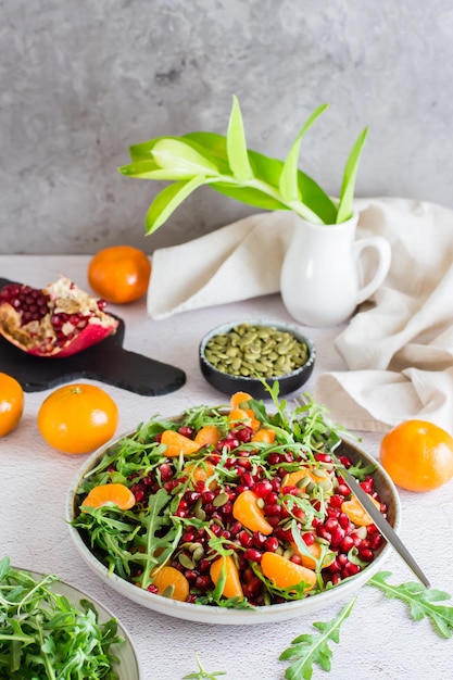 Verzehrfertiger Obstsalat aus Granatapfel, Mandarine, Rucola und Kürbiskernen in einem Teller auf dem Tisch. Organisches vegetarisches Essen.