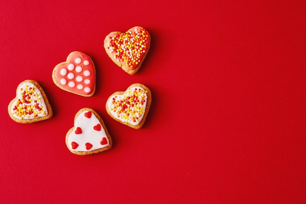 Verziert mit Zuckerglasur und glasierten Herzformplätzchen auf roter Oberfläche mit Kopienraum. Valentinstag-Food-Konzept