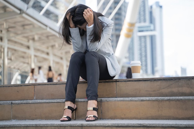 Verzweifelte Geschäftsfrau online besorgt nach Arbeitslosigkeit im Treppenhaus mit den Händen im Kopf