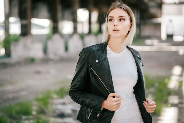 Vestida de camiseta y chaqueta de cuero posando contra la calle