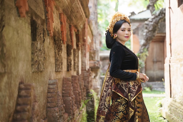 Vestida de kebaya balinés de pie cerca de la valla de la pared de socorro