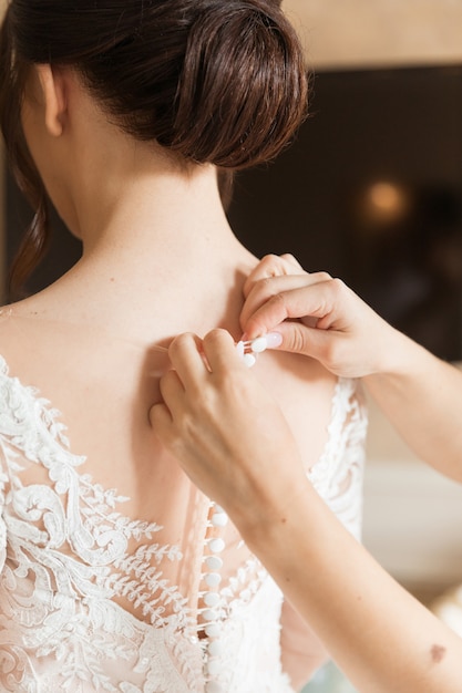 Vestido blanco de la novia a la que la dama de honor ayuda a abotonarse