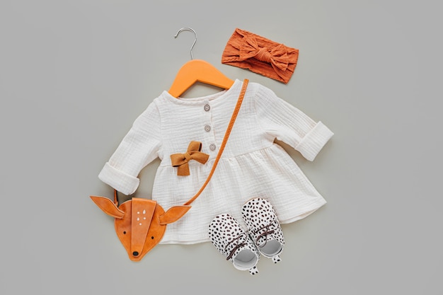Vestido branco com bolsa infantil no cabide e sapatos. Conjunto de roupas de bebê e acessórios para a primavera, outono ou verão em fundo rosa. Roupa de moda infantil. Camada plana, vista superior