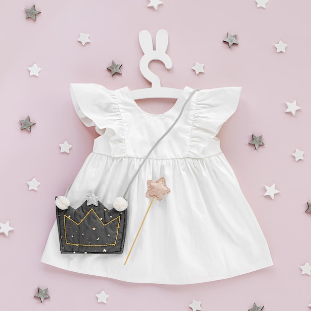 Vestido branco com forma de bolsa infantil de coroa em cabide fofo com orelhas de coelho. Conjunto de roupas de bebê e acessórios para a primavera ou verão em fundo rosa. Roupa de moda infantil. Camada plana, vista superior