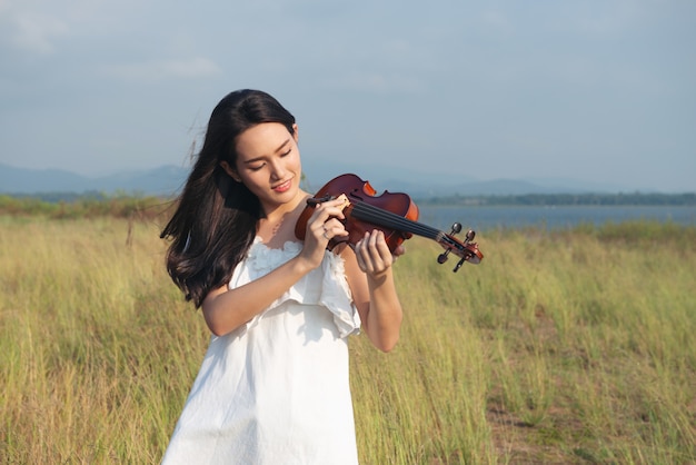 Vestido branco da menina bonita da ásia que joga em um violino