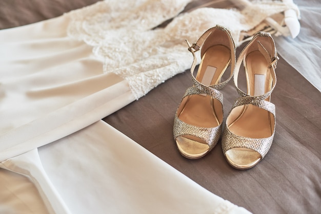 Vestido de casamento elegante branco e sapatas que encontram-se na cama.