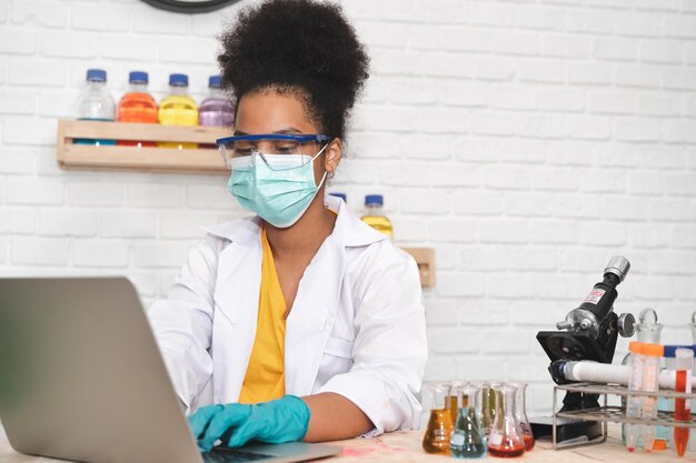 Vestido e máscara para crianças com cabelo afro, usar um laptop com produtos químicos em vidros