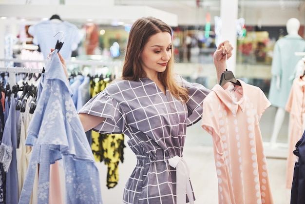 Este vestido es perfecto. Joven y bella mujer sonriente toma una decisión al comprar en una tienda.