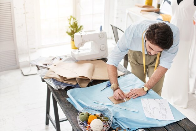 Vestido futuro. Modista experta concentrada de pie en la mesa y haciendo un vestido nuevo