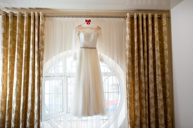 Vestido increíble Longitud total de un hermoso vestido de novia de seda colgado cerca de la ventana Día de la boda