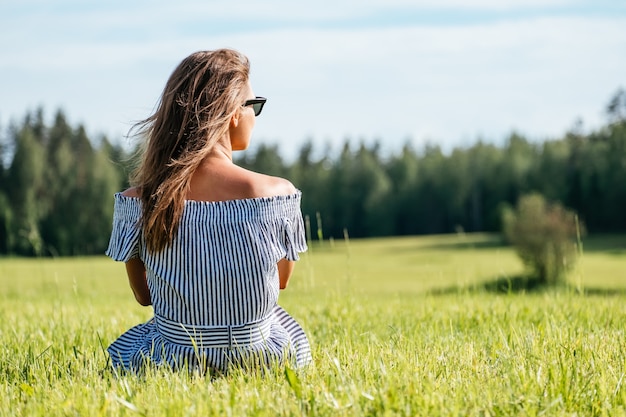 Vestido de mujer sentada en el campo de hierba verde, temporada de verano, relajación en el campo, disfrutando de la naturaleza, concepto de placer