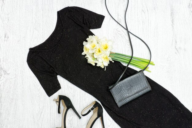 Vestido negro, zapatos, cartera y un ramo de narcisos.