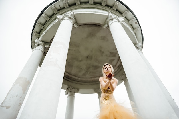 Vestido de niña modelo ángel dorado posando en el bosque cerca de las columnas antiguas