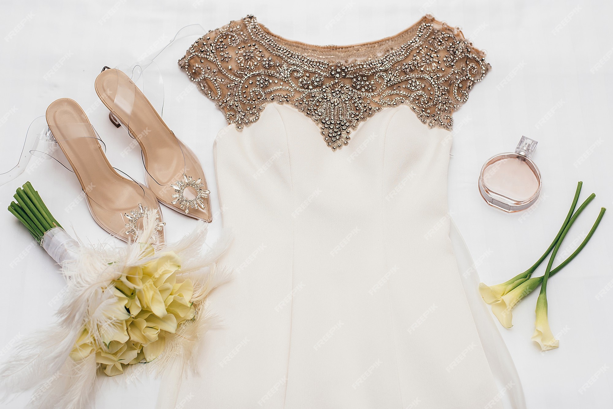 Vestido de novia blanco con doradas se encuentra junto a los zapatos de novia decorados con piedras junto a amarillas y perfume chanel | Foto Premium