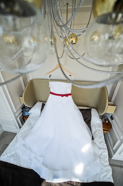 Vestido de novia blanco de la novia colgada de la lámpara de araña en la habitación del hotel