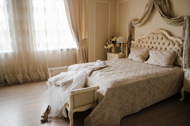 El vestido de novia está en la habitación de la cama. Zapatos beige de la boda.