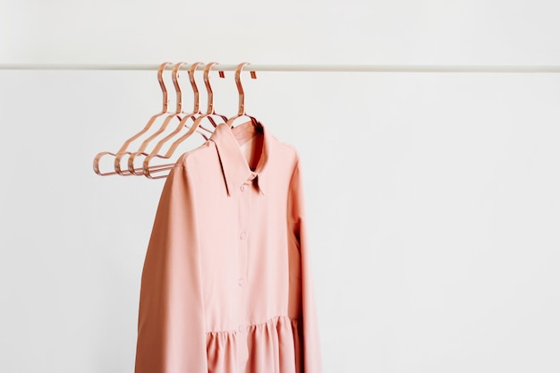 Vestido rosa pálido com cabides metálicos em fundo branco.