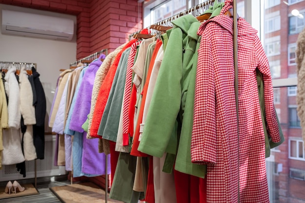 Vestidos femininos coloridos, jaquetas, calças e outras roupas em cabides em uma loja de varejo.