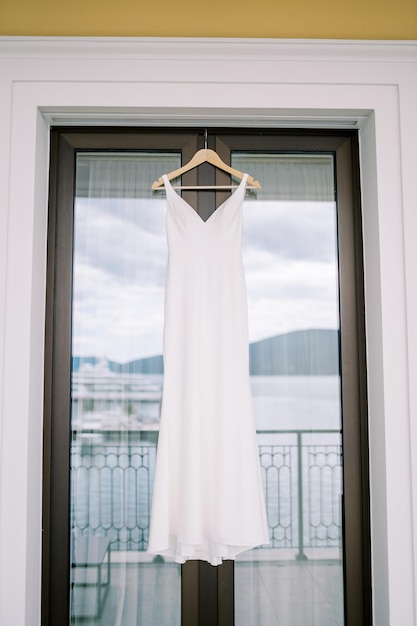 Foto vestuário de noiva pendurado em um gancho em uma porta de varanda de vidro