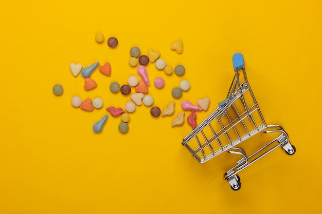 Veterinär-Tabletten von Vitaminen mit verschiedenen Formen für Katzen und Einkaufswagen auf einem gelben