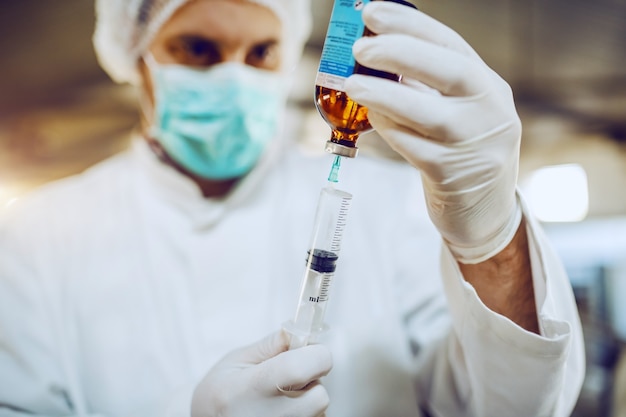 Veterinário em uniforme de proteção e com luvas de borracha enchendo a seringa com a vacina.