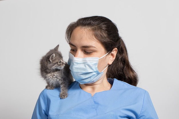 Un veterinario con máscara protectora y uniforme y un pequeño gatito gris.