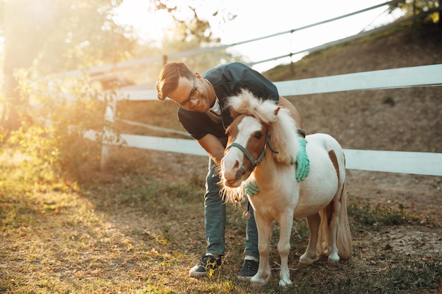 Veterinario de sexo masculino atractivo joven que examina y alimenta el pequeño caballo adorable del pony.