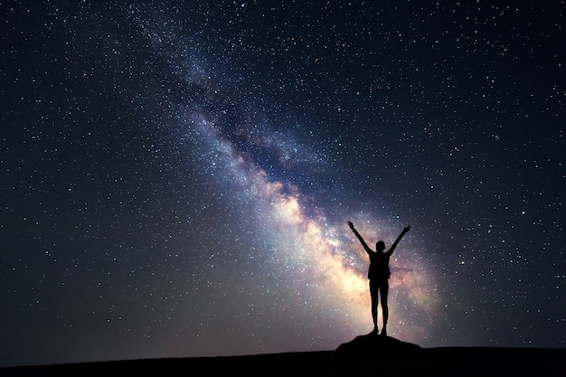 Via Láctea. Céu noturno com estrelas e a silhueta de uma mulher feliz com mochila e braços erguidos. Fundo do espaço