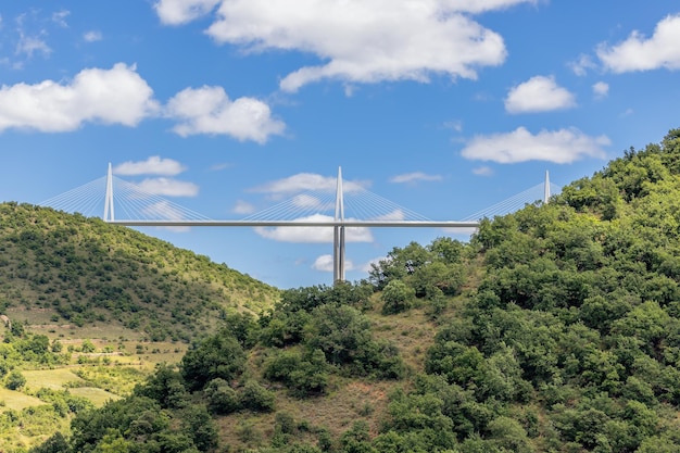 Viaducto de Millau acompañado de una exuberante vegetación en el suelo y un impresionante cielo azul con nubes blancas