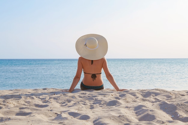 Viagem ao mar. garota em um maiô e chapéu, tomando banho de sol na praia. turista sentado na areia. Vestuário de Lazer. copie o espaço