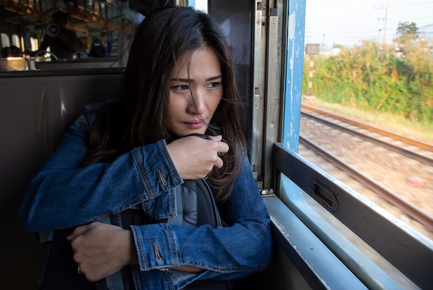 Foto viagem asiática bonita da mulher pelo trem que senta-se perto da janela e que olha através da janela do trem.