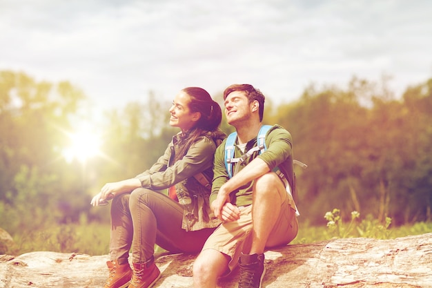 viagem, caminhadas, mochila, turismo e pessoas conceito - casal sorridente com mochilas descansando e desfrutando do sol na natureza